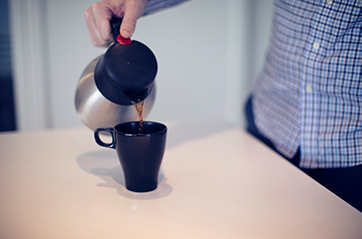 Arm som heller kaffe i en kopp.